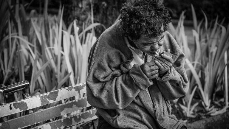 black & white picture of old man, sitting on public bench, smoking